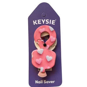 Peut inclure: Un protège-ongles rose avec un motif de cœurs et le texte "KEYSIE" et "Nail Saver" sur un fond violet.