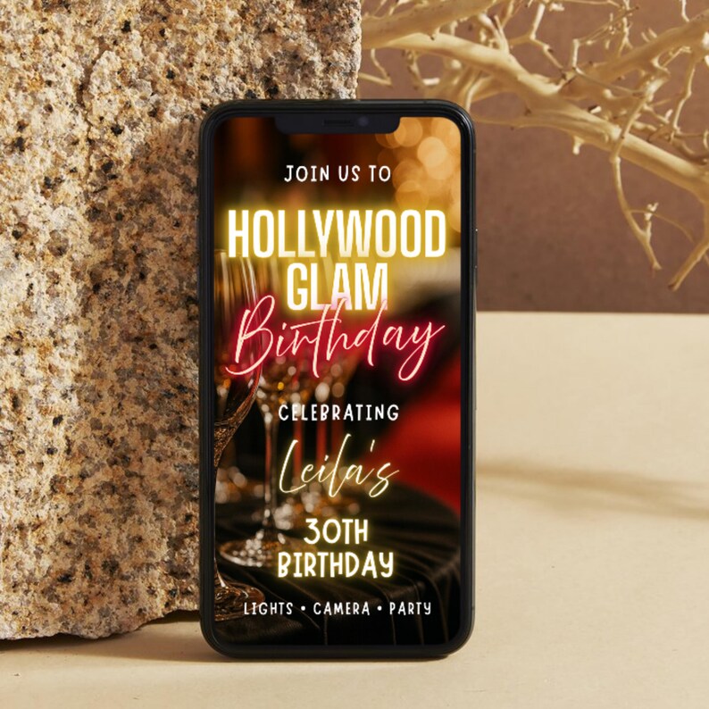 May include: A smartphone displays a Hollywood Glam Birthday invitation. The invitation features gold and red text, including "Hollywood Glam Birthday" and "Celebrating Leila's 30th Birthday." The background includes champagne flutes.