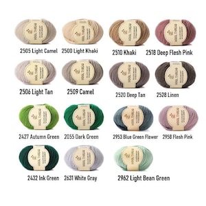 K&ouml;nnte beinhalten: Eine Sammlung von vierzehn ovalen Wollkn&auml;ueln in verschiedenen Farben, jedes mit einem beigen Papieretikett mit der Aufschrift WOOL THREAD. Die Farben umfassen Nuancen von Kamel, Khaki, Rosa, Beige, Gr&uuml;n, Grau und Blau, angeordnet in Reihen.