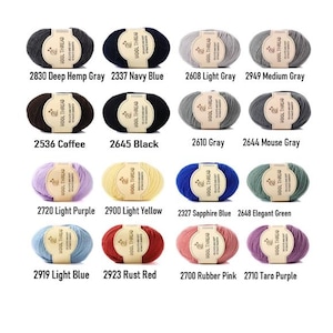 K&ouml;nnte beinhalten: Eine Sammlung von sechzehn Garnkn&auml;ueln in verschiedenen Farben, jedes mit einem beigen Papieretikett mit der Aufschrift WOOL THREAD. Die Farben umfassen Deep Hemp Gray, Navy Blue, Light Gray, Medium Gray, Coffee, Black, Gray, Mouse Gray, Light Purple, Light Yellow, Sapphire Blue, Elegant Green, Light Blue, Rust Red, Rubber Pink und Taro Purple.