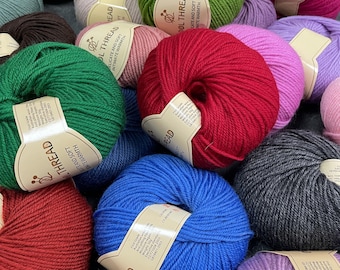 Puede incluir: Una colección de ovillos de lana de colores, cada uno con una etiqueta que dice "Wool Thread, Delicate and Soft, Intimate Warmth".