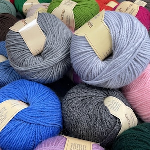 K&ouml;nnte beinhalten: Eine Ansammlung runder Wollkn&auml;uel in verschiedenen Farben wie Grau, Hellblau, K&ouml;nigsblau, Pink, Gr&uuml;n und Dunkelgrau. Jedes Kn&auml;uel hat ein beiges Papieretikett mit dem in Schwarz gedruckten Text WOOL THREAD, das ein Gewicht von 50g angibt.