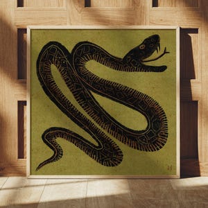 May include: A framed art print showing a stylized illustration of a snake. The snake is black on a muted green background. The artwork is in a wooden frame and is leaning against a wooden wall and floor.