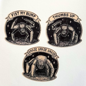 May include: Three black and white stickers with a spider-like creature design. Each sticker has a banner with text: "FIST MY BUMP", "THUMBS UP", and "AMAZE AMAZE AMAZE". The stickers are set against a starry background.