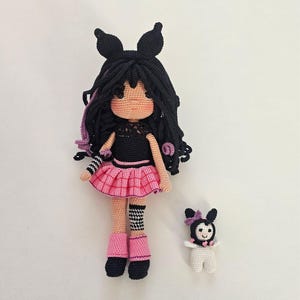 Puede incluir: Muñeca de ganchillo hecha a mano con cabello negro, un top negro y una falda plisada rosa. La muñeca tiene botas negras y una muñeca más pequeña a juego. La muñeca más grande mide unos 30 cm de alto.