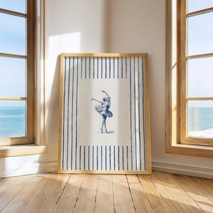 May include: A rectangular framed wall art piece featuring a centered blue ink illustration of a ballet dancer in a tutu. The artwork is set against a cream-colored background with vertical blue stripes framing the central figure on the sides.