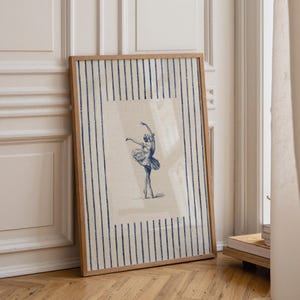 May include: A framed rectangular wall art print featuring a blue ink sketch of a ballerina in a tutu on a light beige background. The print is bordered by a pattern of vertical blue stripes on the left and right sides within the wooden frame.
