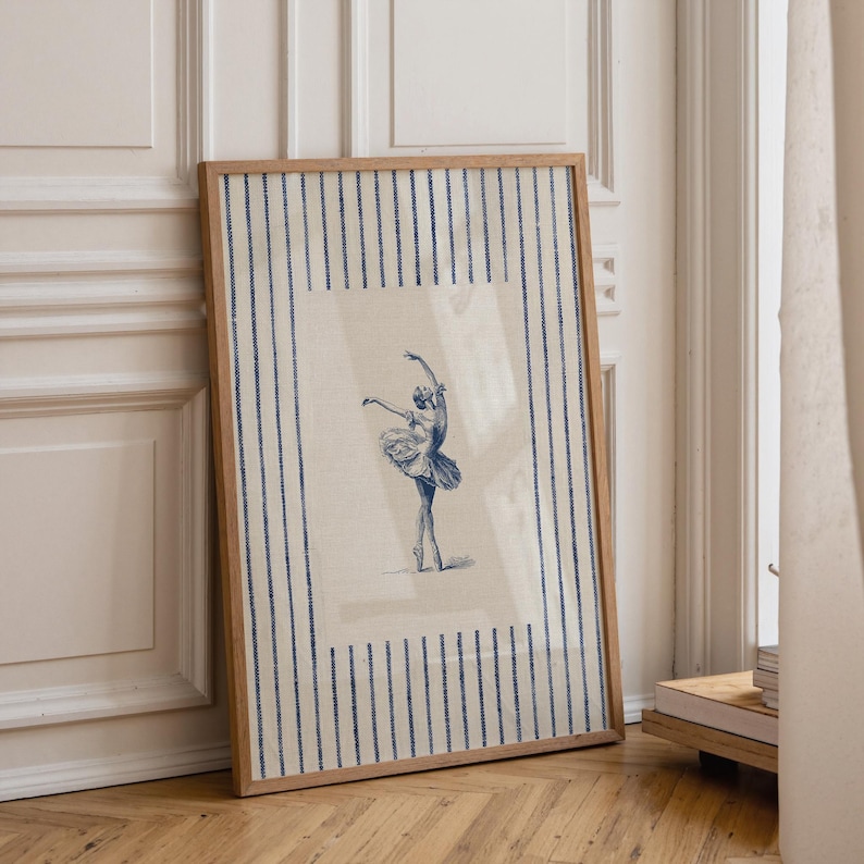 May include: A framed rectangular wall art print featuring a blue ink sketch of a ballerina in a tutu on a light beige background. The print is bordered by a pattern of vertical blue stripes on the left and right sides within the wooden frame.