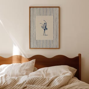 May include: A framed rectangular wall art print featuring a central illustration of a ballet dancer in a tutu, rendered in blue ink on a cream background. The print is surrounded by a border of vertical blue stripes on a cream-colored field.