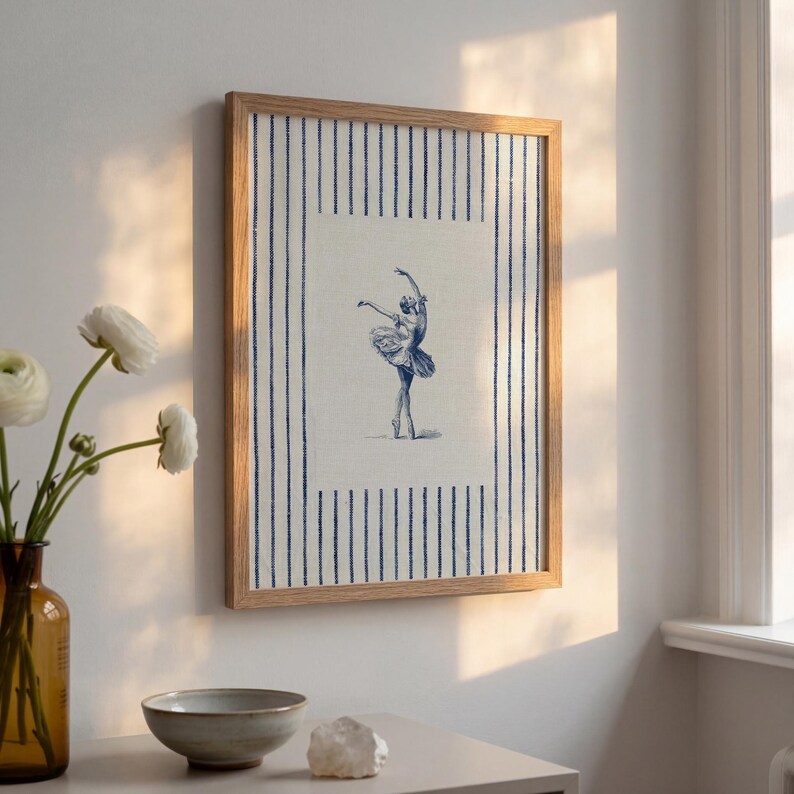 May include: A rectangular wall art piece in a light wood frame featuring a central illustration of a ballerina in a blue ink style. The background of the print has a cream-colored fabric texture with vertical navy blue stripes on the sides.