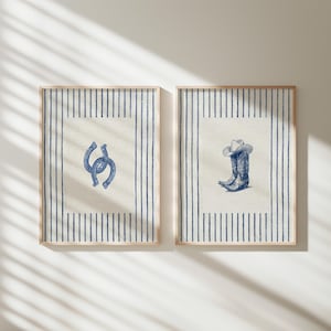 May include: Two framed prints with a rustic theme. One features blue horseshoes, the other a cowboy hat and boots. Both have a cream-colored background with blue vertical stripes and wooden frames.