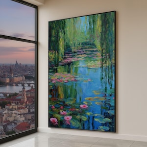 May include: A large framed painting of a water garden scene. Pink water lilies float on a blue pond, reflecting green weeping willows and a small arched bridge. The artwork is displayed in a well-lit room with a city view.