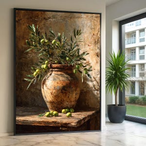 Op de afbeelding: Een ingelijste canvas print toont een stilleven met een rustieke, verouderde terracotta vaas gevuld met olijftakken en groene olijven. De vaas staat op een houten tafel, met verspreide olijven. De achtergrond is een getextureerde, warm getinte muur.