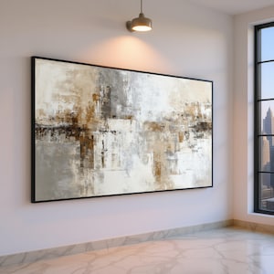 May include: Abstract art piece in a black frame. The artwork features a blend of neutral colors, including white, gray, and brown, creating a textured, layered effect. The painting is displayed on a white wall in a well-lit room with a window.