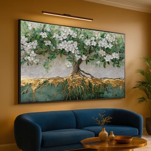 Könnte beinhalten: Großformatige gerahmte Kunst mit einem Baum mit weißen Blüten und goldenen Akzenten. Die Wurzeln des Baumes sind goldfarben vor einem türkisfarbenen und strukturierten Hintergrund. Das Kunstwerk hängt über einem blauen Sofa.