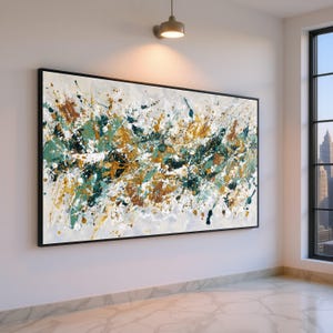 Könnte beinhalten: Abstrakte Kunstmalerei mit schwarzem Rahmen. Das Kunstwerk zeigt einen weißen Hintergrund mit Farbspritzern in Türkis, Gold, Braun und Schwarz. Das Gemälde wird an einer weißen Wand in einem Raum mit Fenster ausgestellt.