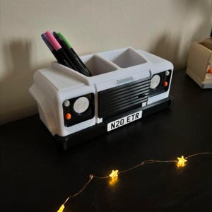 May include: White desk organiser shaped like a Land Rover Defender with a black grille and the number plate "N20 ETR".