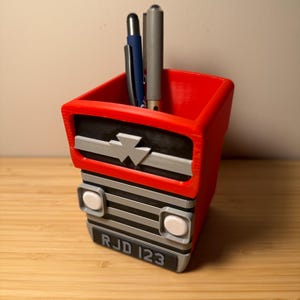 May include: Red and black 3D printed desk organiser shaped like a vintage truck with the number plate "RJD 123".