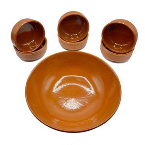 Könnte beinhalten: Satz mit fünf Terrakotta-Schalen, darunter eine große Servierschale und vier kleinere Schalen. Die Schalen sind alle in einem satten Orangebraun gehalten und haben eine glatte, leicht glänzende Oberfläche.