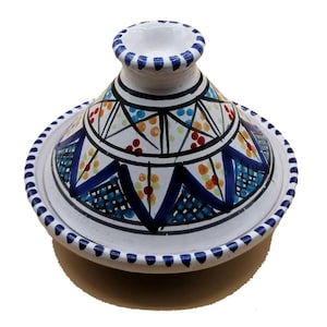 May include: A white ceramic tagine pot with a conical lid and a wide, shallow base. The lid and base are decorated with geometric patterns in blue, orange, yellow, and black. The rim of the base and the top of the lid have a blue dotted design.