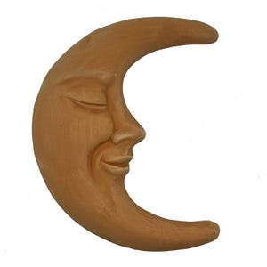 May include: A terracotta crescent moon sculpture with a smiling face. The moon is a light brown colour and has a smooth, slightly textured surface.