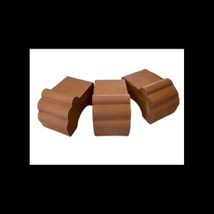 Op de afbeelding: Drie terracotta-kleurige, decoratieve architecturale elementen. Elk stuk heeft een gebogen, geschulpte rand en een rechthoekig lichaam. De stukken zijn in een groep gerangschikt, die hun ontwerp en textuur laten zien. De elementen lijken van klei te zijn.