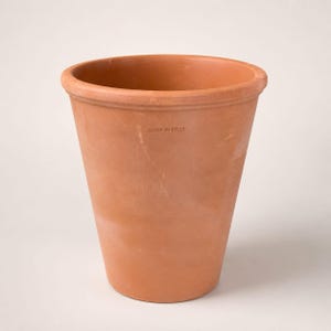 Op de afbeelding: Een terracotta plantenpot met een taps toelopende cilindrische vorm en een dikke, afgeronde rand. Het oppervlak heeft een matte, aardse oranje kleur met subtiele kleurnuances. De tekst MADE IN ITALY staat duidelijk in de zijkant gestempeld.