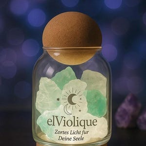 Könnte beinhalten: Ein Glasbehälter mit Holzsockel und Korkdeckel, gefüllt mit grünen und weißen Kristallen. Auf dem Glas steht "elViolique" und "Zartes Licht fur Deine Seele". Der Hintergrund ist ein verschwommener Mix aus Lila und Blau.