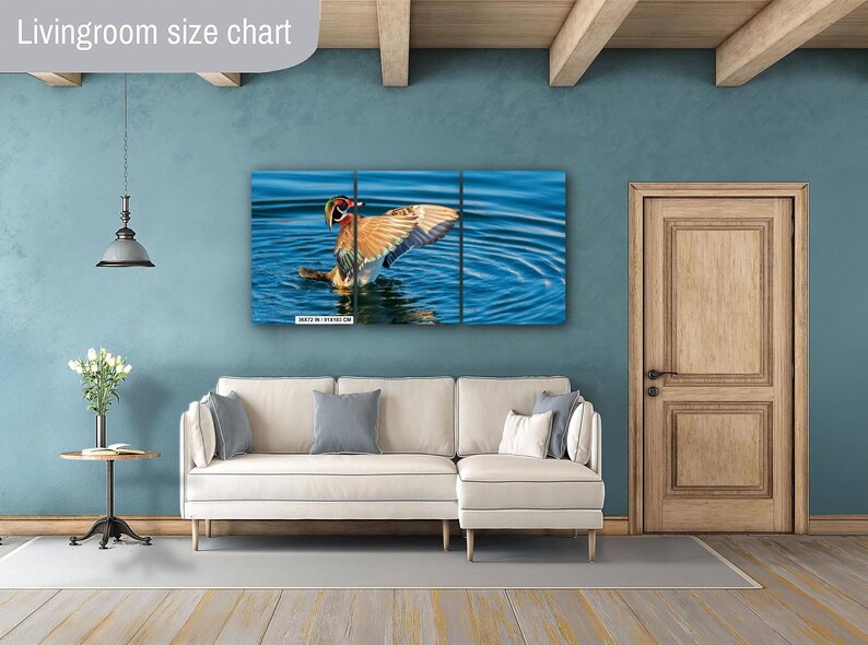 May include: A three-panel canvas print of a duck in water, with its wings spread. The artwork is displayed above a white sofa in a living room setting. The text "Livingroom size chart" is in the upper left corner.