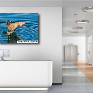 May include: A framed canvas print of a duck with outstretched wings in blue water. The duck has brown, orange, and white feathers. The print is labeled "30X40 IN / 76X102 CM". The image is displayed on a white wall in a modern office setting.
