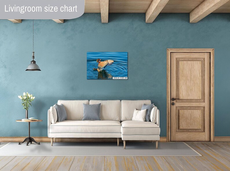 May include: A framed print of a bird in water, with wings spread, is displayed above a white sofa. The room has a teal wall, a wooden door, and a wooden ceiling. A side table with a lamp and a vase of flowers is in the foreground.