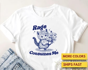 Puede incluir: Camiseta blanca con una ilustración azul de un gatito sosteniendo flores, con el texto "Rage Consumes Me" en azul. La camiseta se muestra con vaqueros azules y un sombrero de paja.