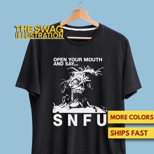 May include: Black t-shirt with a white graphic of a screaming face and the text "OPEN YOUR MOUTH AND SAY..." and "SNFU". The shirt is hanging on a wooden hanger.