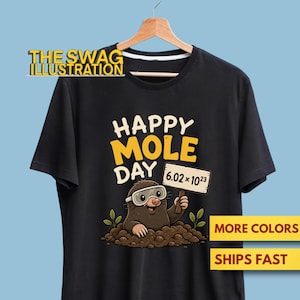 Puede incluir: Una camiseta negra con el gráfico de un topo marrón con gafas de seguridad, saliendo de un montón de tierra. El topo sostiene un cartel que dice 6.02 x 10^23. Sobre el topo, el texto dice HAPPY MOLE DAY en letras grandes amarillas y blancas.