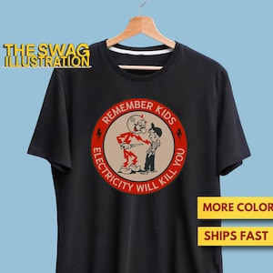 Puede incluir: Camiseta negra con un gráfico circular rojo que presenta un personaje de dibujos animados sosteniendo un cuchillo y el texto "Remember Kids Electricity Will Kill You".