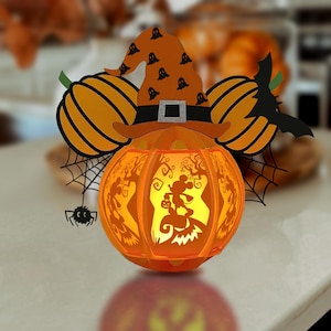 May include: A Halloween-themed pumpkin lantern with a witch hat and Mickey Mouse silhouette. The orange pumpkin has cut-out designs and is lit from within. Decorative pumpkins, a spider, and a bat are also included in the design.