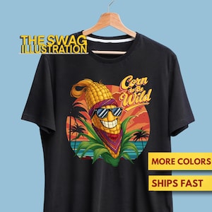 Op de afbeelding: Zwart T-shirt met een cartoon maïskarakter met een zonnebril en bandana, met de tekst "Corn to Be Wild" in een tropische scène. Het logo van The Swag Illustration staat bovenaan.