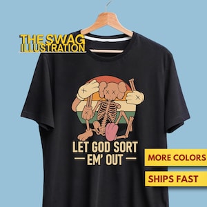 May include: Black t-shirt featuring a cartoon skeleton with a pink tongue, holding sticks, and a retro sunset design. The text "LET GOD SORT - EM' OUT" is below the graphic. The shirt also has the text "MORE COLORS" and "SHIPS FAST".