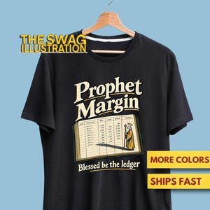 May include: A black short-sleeve t-shirt featuring a graphic of an open ledger with the text "Prophet Margin" above it and "Blessed be the ledger" below. The ledger includes a small illustration of a figure with a staff and a halo.