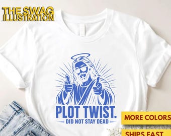 May include: A white short-sleeved t-shirt featuring a blue graphic of a figure with a halo and sunglasses pointing forward with both hands. Below the graphic, the text reads PLOT TWIST. DID NOT STAY DEAD. The shirt is displayed with blue denim.
