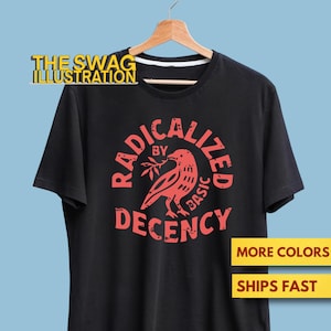 May include: Black t-shirt with a red graphic of a bird holding a branch, and the words "RADICALIZED BY BASIC DECENCY." The text "THE SWAG ILLUSTRATION" is above the shirt. The shirt is hanging on a wooden hanger.