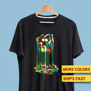 May include: Black t-shirt featuring a colorful, melting Rubik's Cube graphic. The design shows the cube with its colors dripping down the shirt. The shirt also has the text "MORE COLORS" and "SHIPS FAST".