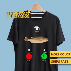 May include: Black t-shirt featuring a fish graphic and the text "fih Calling...". The design includes a fish illustration and phone interface icons for decline and accept. The shirt is hanging on a wooden hanger.