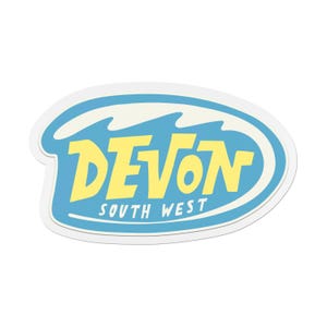 Puede incluir: Una pegatina con un diseño ovalado azul con la palabra "Devon" en amarillo, con "South West" debajo. El diseño incluye formas de olas blancas en la parte superior, todo delineado en blanco.