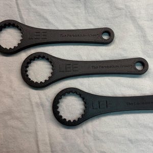 Puede incluir: Tres llaves negras con una cabeza dentada circular y un mango con un agujero. La palabra "LEE" está impresa en el mango. El texto "The Parthenon Arms" también está impreso en el mango.