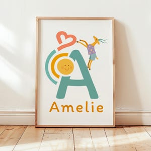 Könnte beinhalten: Ein gerahmter Kunstdruck mit einem großen türkisfarbenen Buchstaben A, einer gelben Sonne, einem korallenroten Herz und einer stilisierten Ziege in einem violetten gepunkteten Oberteil. Der Name Amelie steht in orangefarbenen Buchstaben unten.