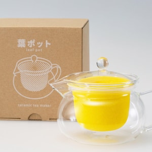 Puede incluir: Una tetera de vidrio transparente con un infusor de cerámica amarillo. La tetera tiene una tapa y un asa. La caja en el fondo dice "Leaf Pot" y "Ceramic Tea Maker".