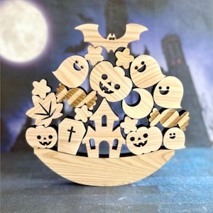 Może przedstawiać: Drewniana dekoracja na Halloween z nietoperzem, duchami, dyniami, cukierkami i nawiedzonym domem. Elementy ułożone są na drewnianej podstawie, z pełnią księżyca i upiornym tłem.
