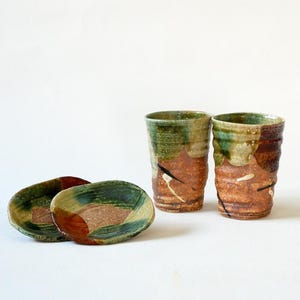May include: Two green and brown ceramic cups with a textured design and two matching small plates.