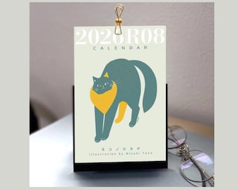 Puede incluir: Calendario de escritorio con una ilustración estilizada de un gato en verde azulado y amarillo. El calendario muestra el texto "2020 R08 CALENDAR" en la parte superior. Se sujeta con un clip dorado y se apoya en una base negra.